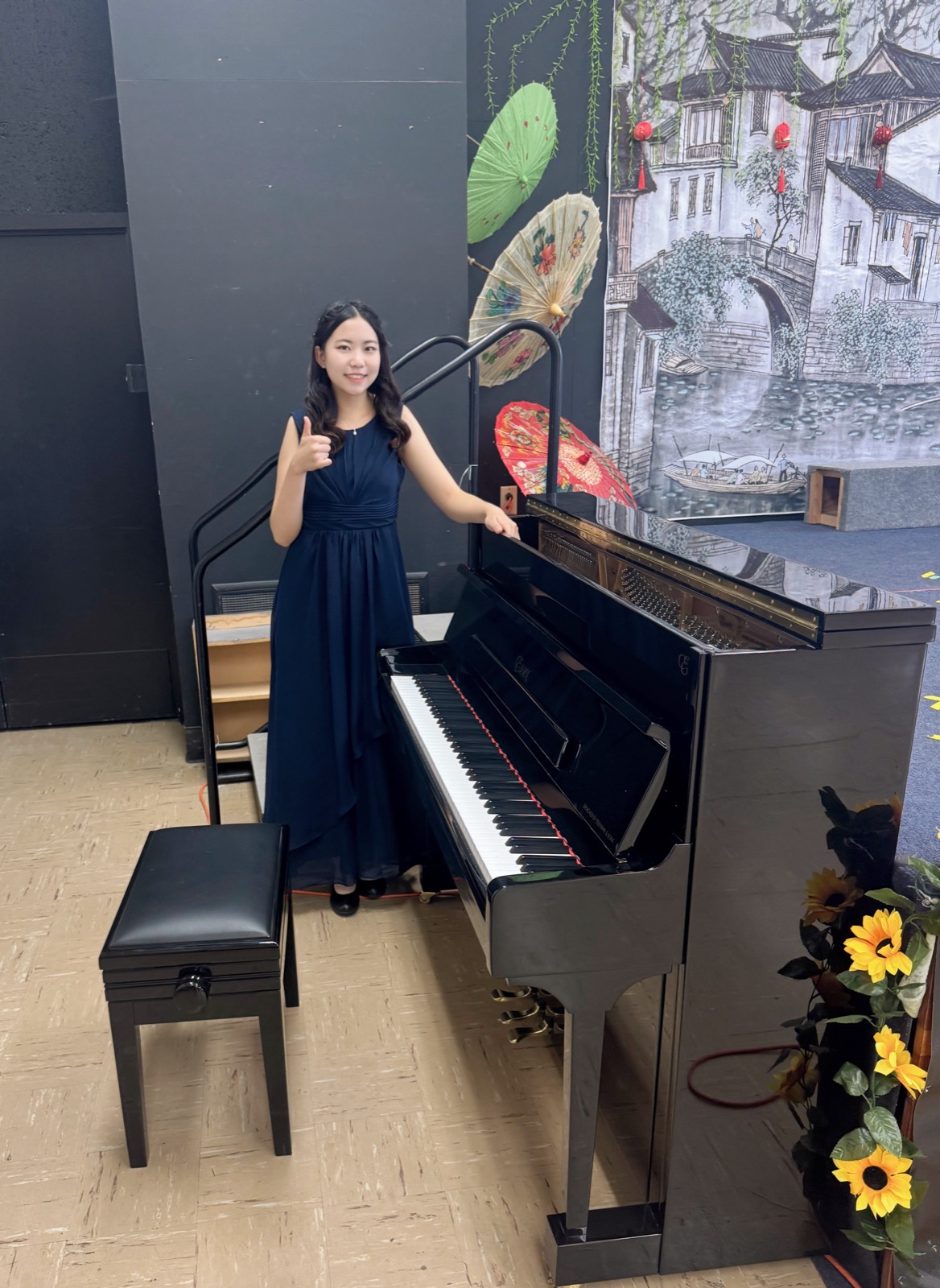 Meining Wu standing beside the newly delivered Essex EUP-111 upright piano in the hall at Enlighten Enrichment School, donated by Elena Rodighiero