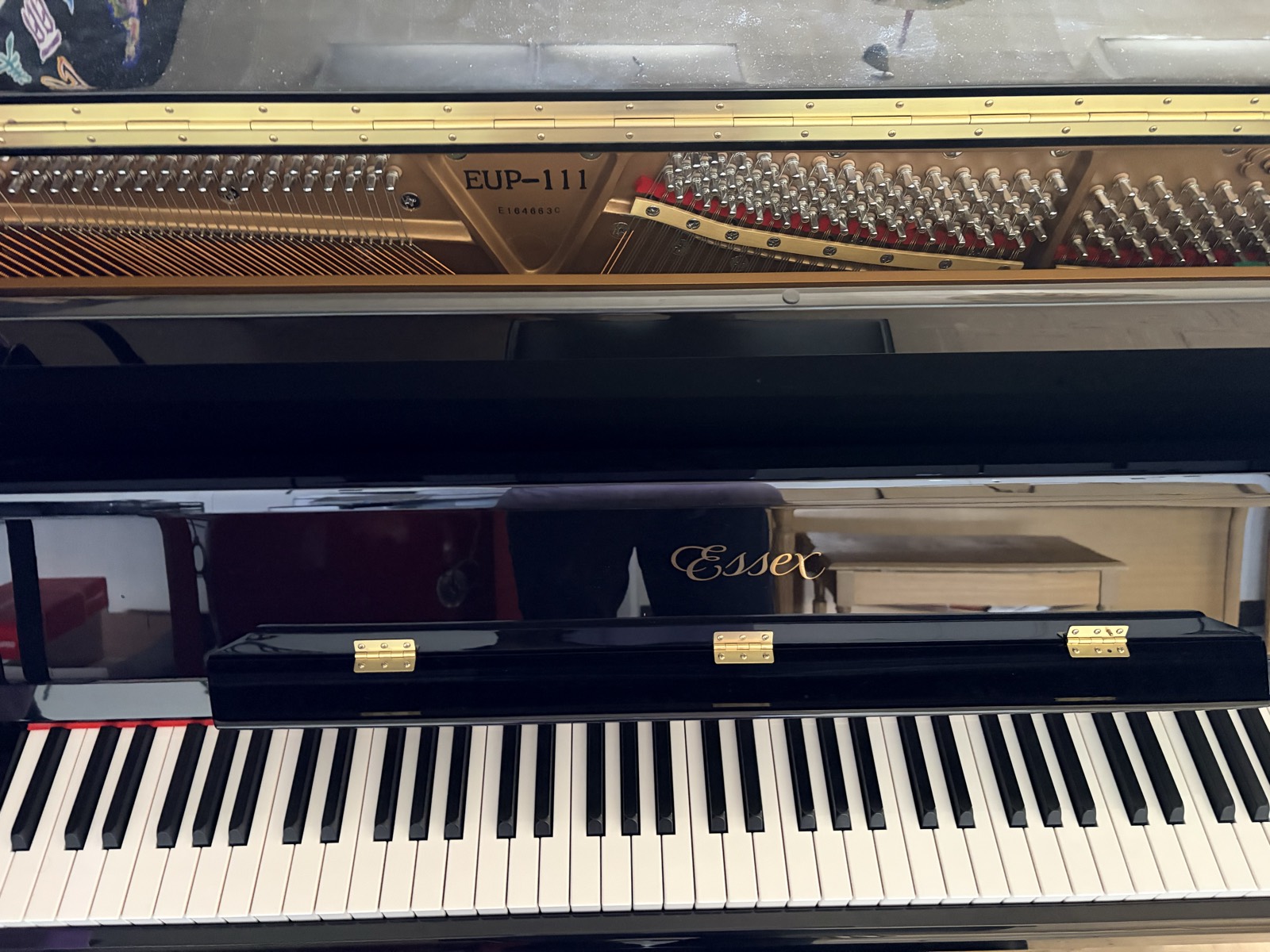 Close-up of the donated Essex EUP-111 upright with the lid open, showing the gold-lettered Essex name above the keyboard and the strings and tuning pins inside